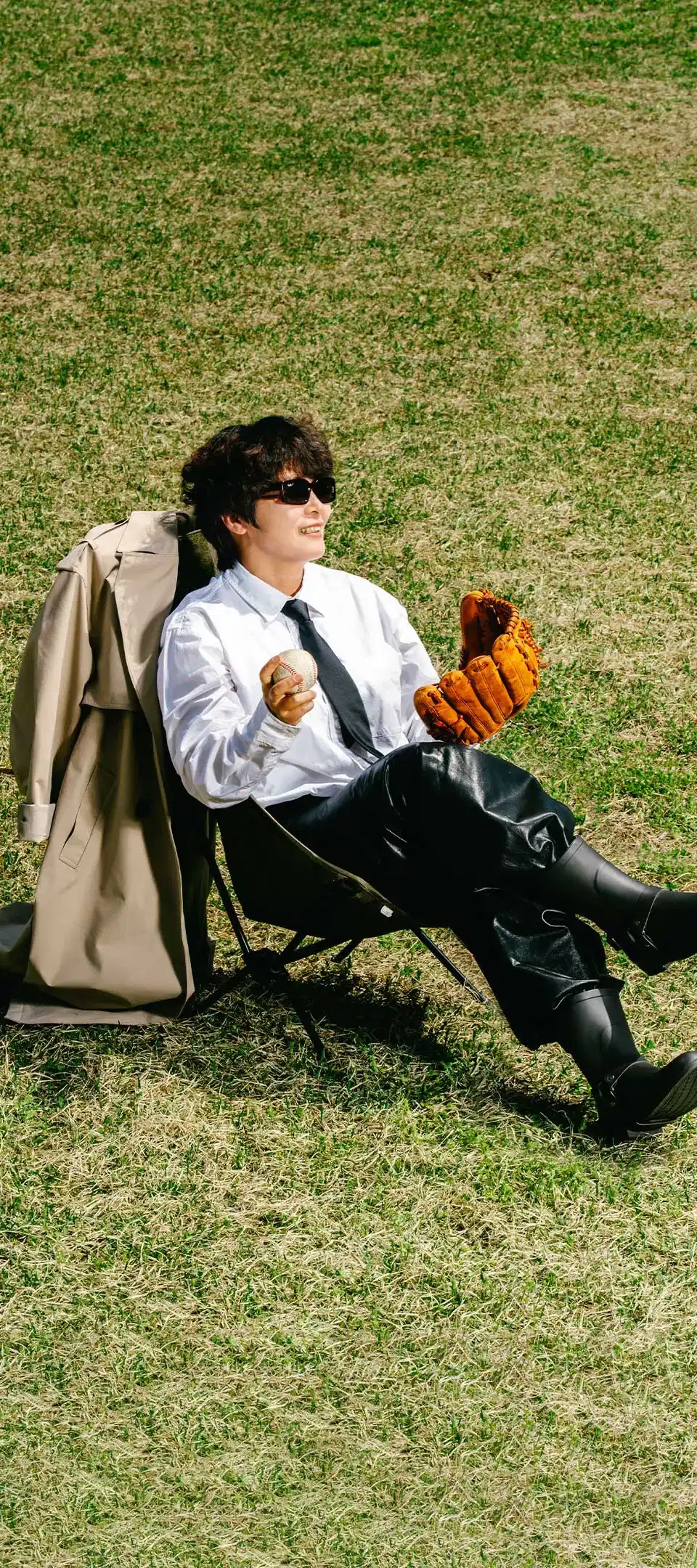 트렌치코트를 벗은 채, 잔디밭에서 캠핑 의자에 앉아 한 손에는 야구공을 들고 다른 한 손에는 야구 글러브를 끼고 있는 김용자 이장의 사진. 사건을 해결한 듯 여유로운 미소를 짓고 있다.